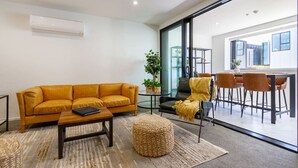 A modern living room with a sofa, coffee table, ottoman, and a dining area with chairs and a table.