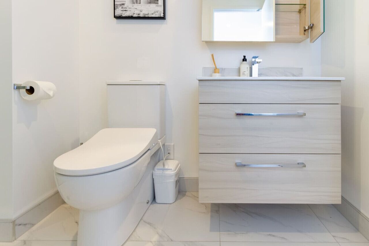 A modern bathroom with a toilet, a sink with a mirror, and a trash bin.