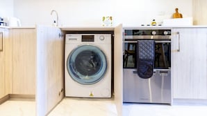Una cocina compacta con lavadora y horno integrados, armarios de madera y piso de baldosas.