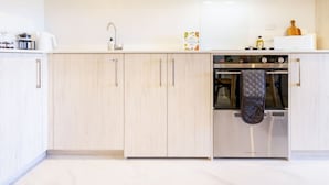 Una cocina moderna con armarios de madera clara, un horno de acero inoxidable y una tetera sobre la encimera.