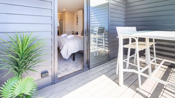 Een moderne kamer met een bed, een tafel en stoelen, plus een schuifglasdeur naar een balkon.