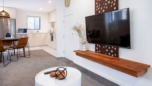 Una cocina moderna con comedor, un televisor de pantalla plana montado en la pared y una mesa redonda de centro con un control remoto.
