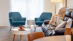 Una sala de estar con un sofá de cuero, dos sillones azules, una mesita auxiliar blanca y una lámpara.