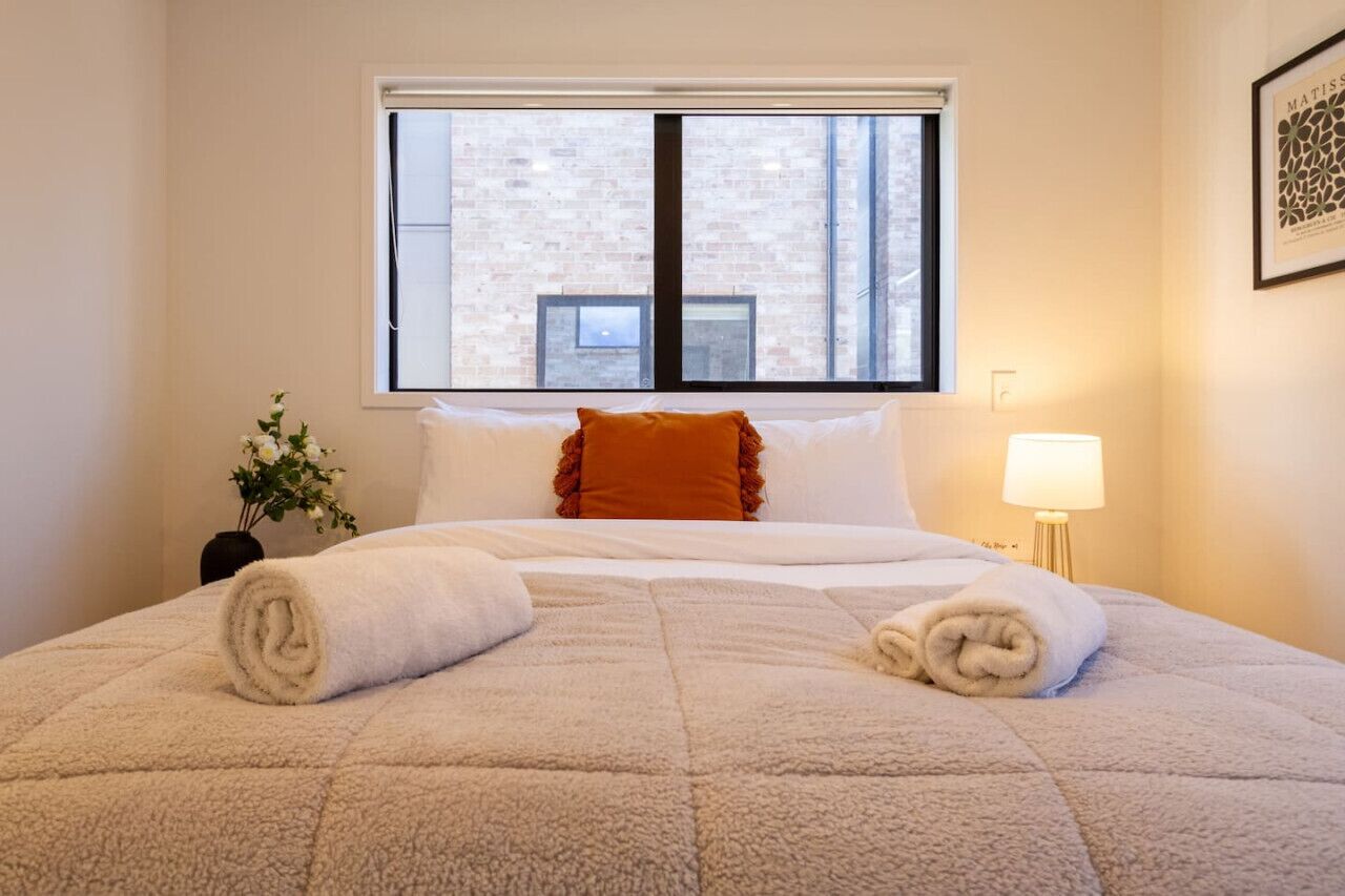 A hotel room with a large bed, a window with blinds, a bedside lamp, and a framed picture on the wall.