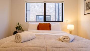 A hotel room with a large bed, a window with blinds, a bedside lamp, and a framed picture on the wall.