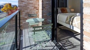 Un balcón con una mesa y sillas, una cama con colcha estampada y una pared de ladrillo.