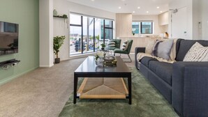 Ein modernes Wohnzimmer mit Sofa, Couchtisch und Fernseher. Ein großes Fenster bietet Blick auf die Straße.