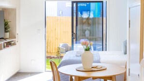 Et moderne køkken med hvide skabe, et spiseområde med et rundt bord og stole, samt en skydedør, der fører ud til en terrasse.