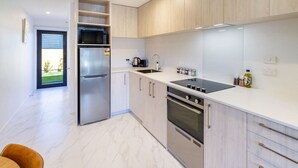 Una cocina moderna con electrodomésticos de acero inoxidable, armarios de madera clara y encimera blanca.