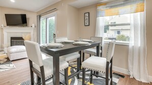 Un coin repas avec une table en bois foncé, des chaises à revêtement blanc et une cheminée.