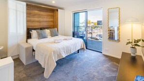 Een moderne slaapkamer met een groot bed, een schuifdeur naar een balkon, een nachtkastje en een spiegel.