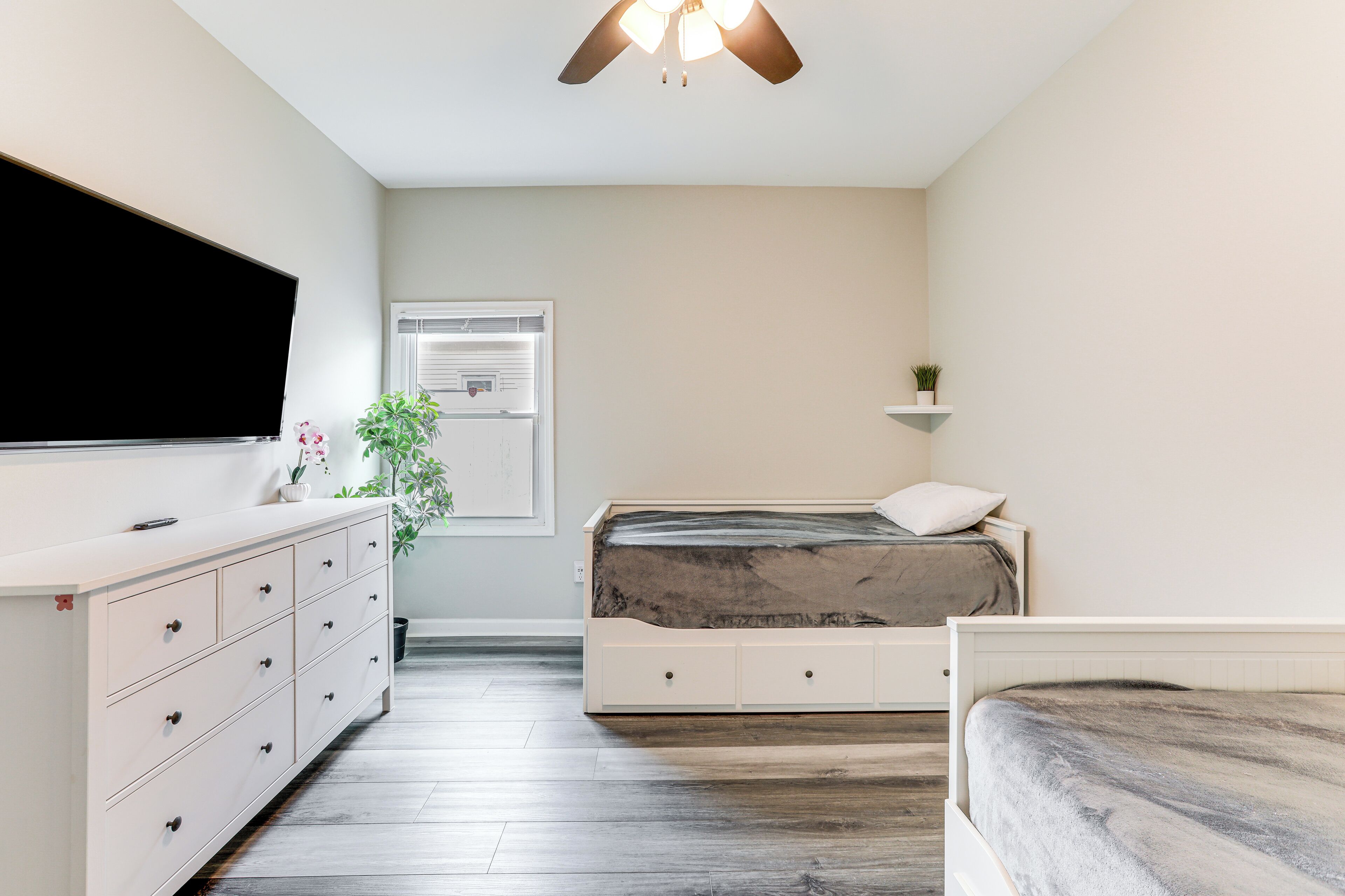 Une chambre à coucher comprenant un lit, une commode, un téléviseur et une fenêtre avec des stores.