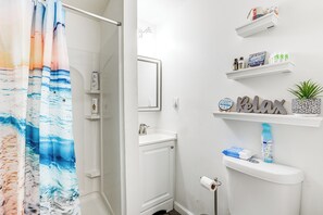 Une salle de bain avec un rideau de douche, un lavabo, des toilettes et des étagères contenant des articles de toilette.