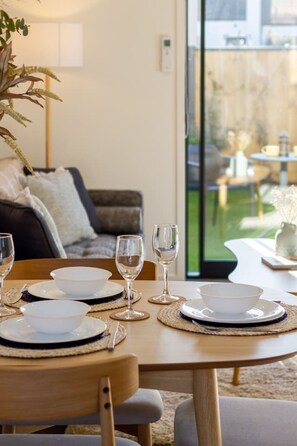 A dining table set with plates, bowls, and wine glasses, with a view of a garden through a large window.