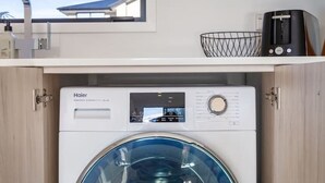 Un lavadero pequeño y moderno con una lavadora Haier, un microondas arriba y una ventana que proporciona luz natural.