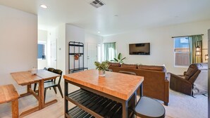 Una sala moderna con una mesa de comedor de madera, un sofá y un sillón reclinable. Hay un televisor montado en la pared y una ventana con cortinas.