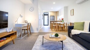 A modern living room with a flat-screen TV, a wooden coffee table, a sofa, and a dining area with a kitchen in the background. - Cozy and Chic in Central Christchurch (Christchurch)