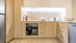 A modern kitchen with wooden cabinets, a built-in oven, and a stainless steel dishwasher. - Cozy and Chic in Central Christchurch (Christchurch)