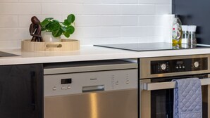 Una cocina moderna con lavavajillas, horno y una encimera con una planta y tabla de cortar.