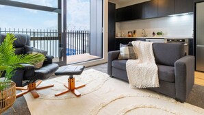 Una sala moderna con un sofá, un sillón y una zona de comedor con una cocina al fondo.