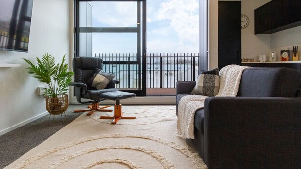 Una sala de estar moderna con sofá, sillón y un amplio ventanal con vistas a un balcón.