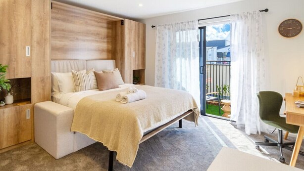 A modern bedroom with a bed, a desk, and a balcony with plants.