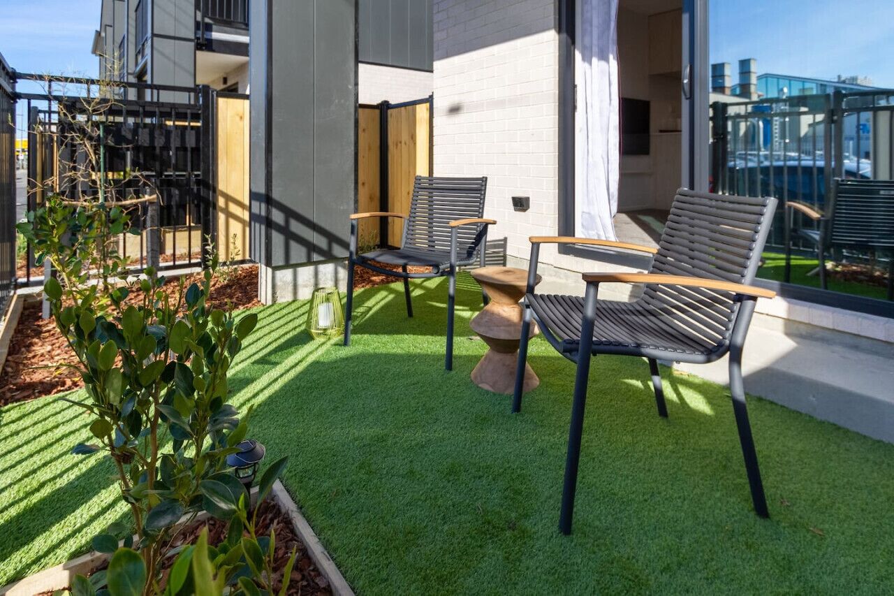 Un espace extérieur moderne aménagé avec du gazon synthétique, des chaises en métal et une petite table.