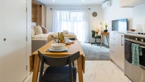A compact hotel room with a dining area, kitchenette, and a bed with a view of the outdoors.