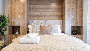A modern bedroom with a large bed, wooden headboard, and bedside tables with plants.