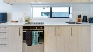 A modern kitchen with light wood cabinets, a built-in oven, a dishwasher, and a window providing natural light.