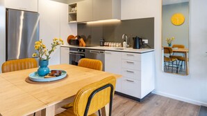 Cozinha moderna com área de jantar, apresentando uma mesa de madeira, cadeiras amarelas e um vaso azul com flores.