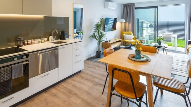 Uma cozinha moderna com eletrodomésticos de aço inoxidável, uma área de jantar com mobiliário de madeira e uma grande porta de vidro deslizante para o exterior.