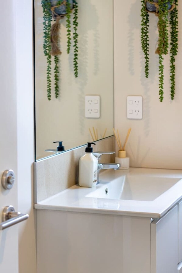 A bathroom with a white sink, a mirror, and hanging green plants.