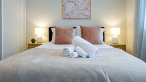A neatly made bed with pillows, a rolled towel, and two bedside lamps.