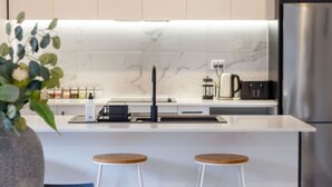A modern kitchen with a white marble backsplash, stainless steel appliances, and two wooden stools.