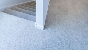 A hallway with a carpeted staircase leading to a bedroom with a bed and a window.