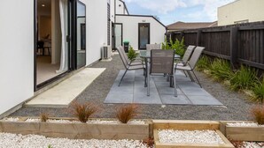A patio with a table and chairs, a sliding glass door, and a wooden fence.