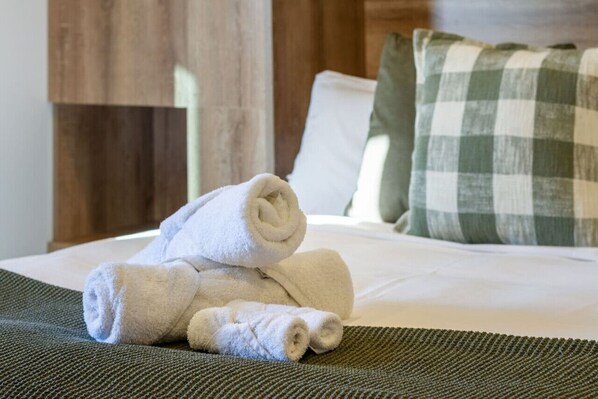 A neatly made bed with white linens and a green checkered pillow.