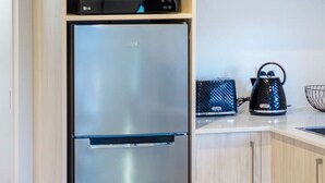 A compact kitchen with a built-in refrigerator, a kettle, and a small shelf with glasses and a plant. - Single Level Studio Escape on Wilmer St - Central (Christchurch)