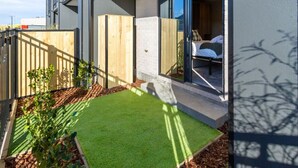 A modern building with a balcony, a small garden area with artificial grass, and a wooden fence. - Single Level Studio Escape on Wilmer St - Central (Christchurch)