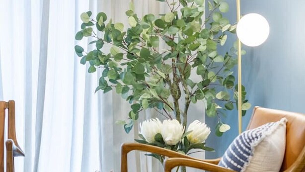 Un salón acogedor con una silla de madera, una mesita auxiliar, un jarrón con flores y una lámpara de pie.