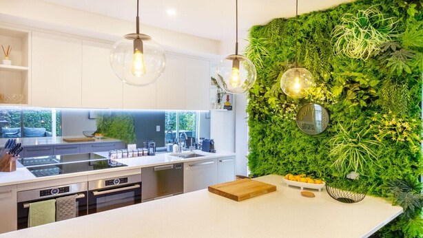 A modern kitchen with a white countertop, stainless steel appliances, and a green vertical garden wall.