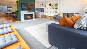 A modern living room with a fireplace, a grey sofa, and a dining area with chairs.