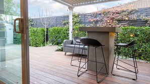 An outdoor patio with a concrete bar area, two black bar stools, and a grey sofa.