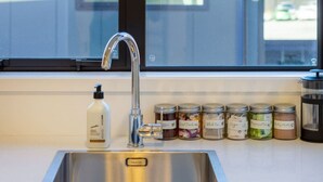 Una cocina con un lavamanos de acero inoxidable, un grifo y una fila de frascos etiquetados con diferentes condimentos.