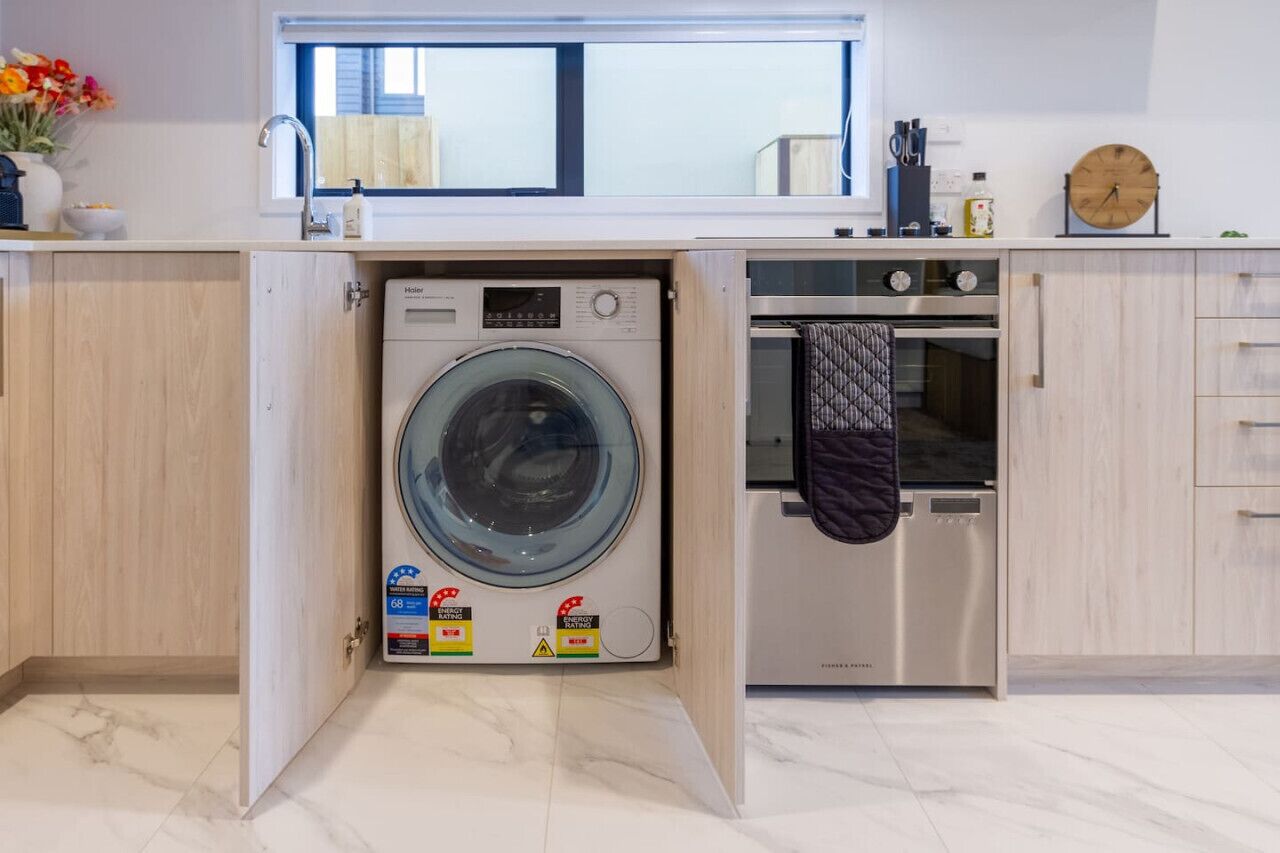 Een compacte keuken met een ingebouwde wasmachine en droger, een roestvrijstalen oven, en een raam boven de gootsteen.