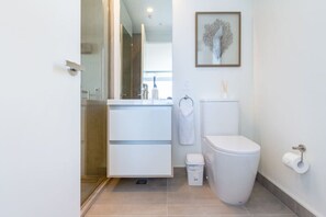 Casa de banho moderna com cabine de duche em vidro, sanita branca e espelho minimalista com porta-toalhas.