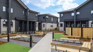 A modern residential complex with multiple apartment buildings, a central courtyard with benches, and a well-maintained lawn. - Trendy Ground Floor Studio  - Central Cafes (Christchurch)