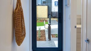 A modern hallway with a glass door leading outside, a wooden wall art piece, and a textured rug. - Trendy Ground Floor Studio  - Central Cafes (Christchurch)
