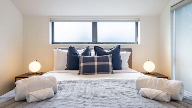 A neatly made bed with a quilted blanket, two pillows, and two bedside lamps. - Urban comfort and parking near Avebury Park (Christchurch)